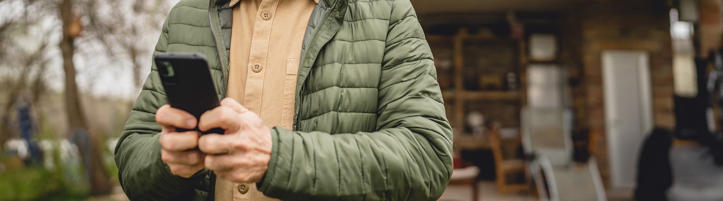 Personne en veste matelassée utilisant un smartphone dans un environnement extérieur flou